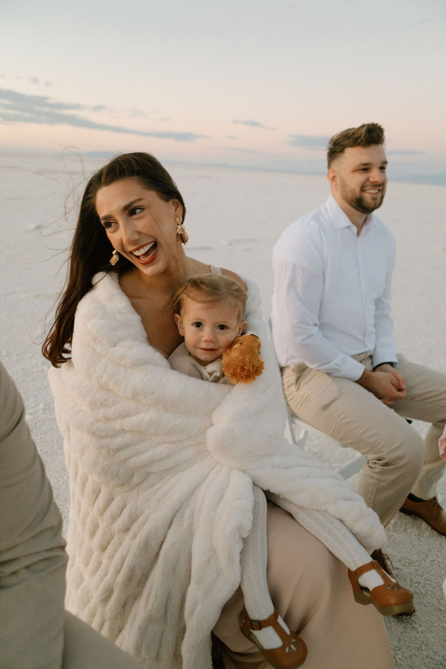 A family moment captured on salt flats at sunset with a small child holding a teddy bear.