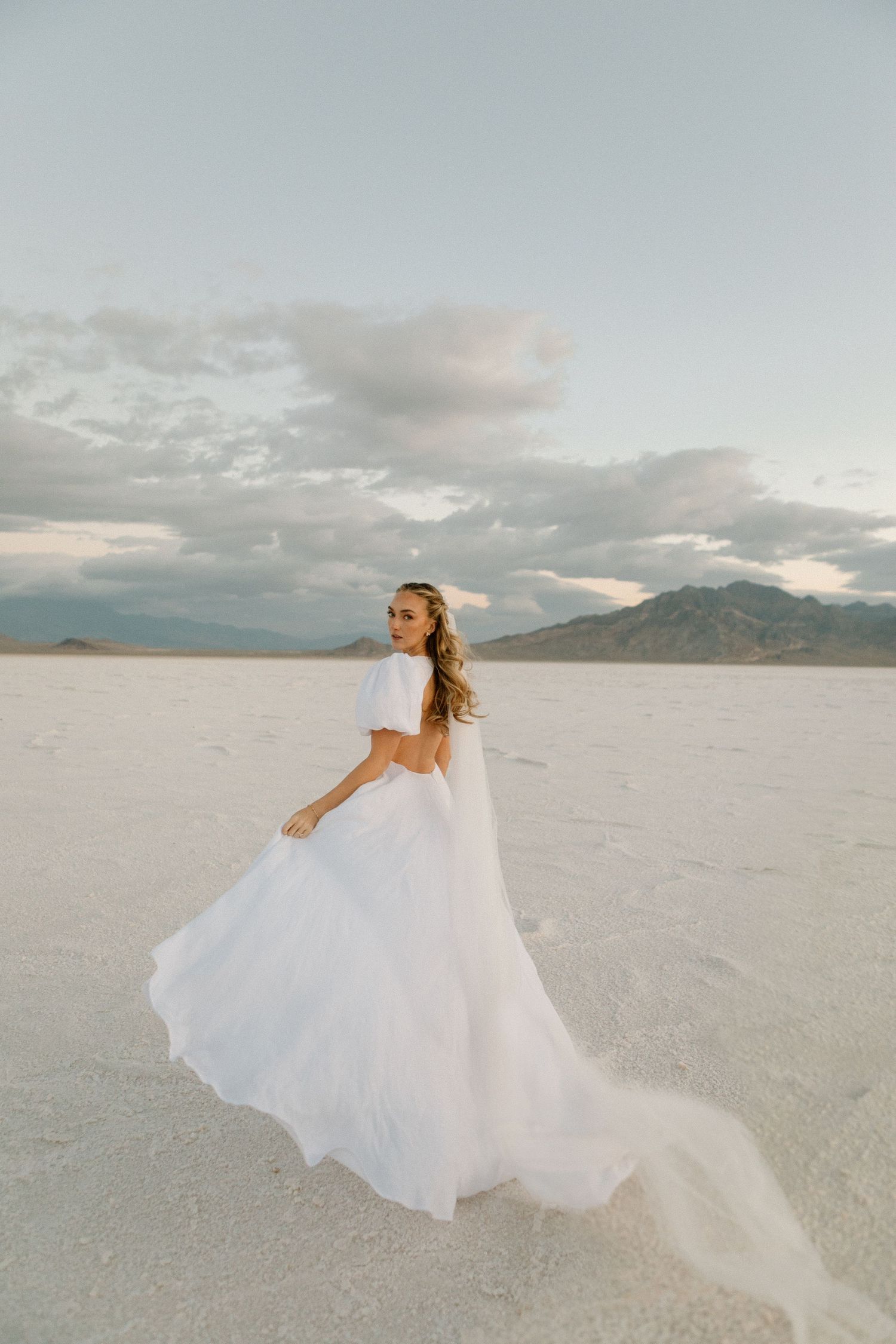 A flowing white dress catches the wind on a stark salt flat landscape.