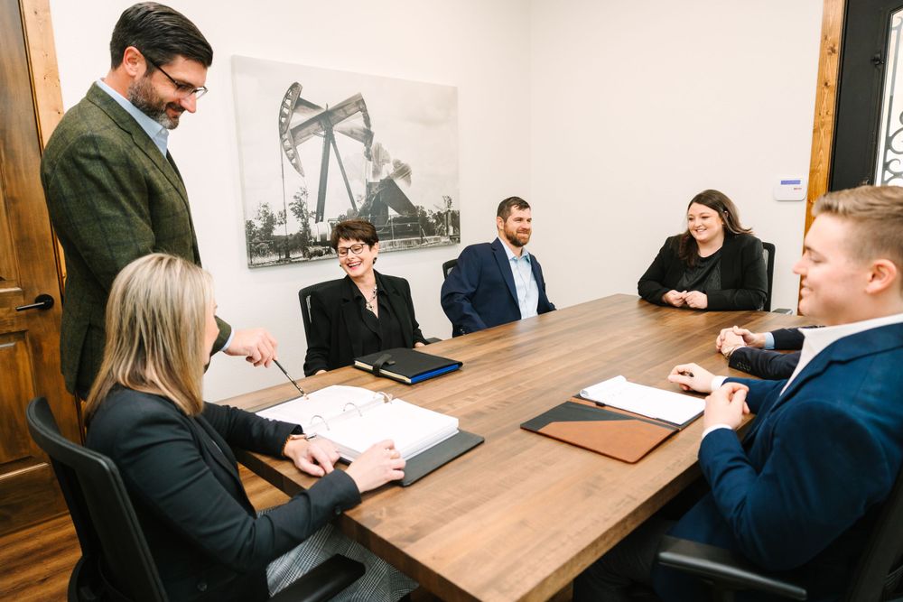 Business professionals meet in a conference room with an oil derrick photograph on the wall.