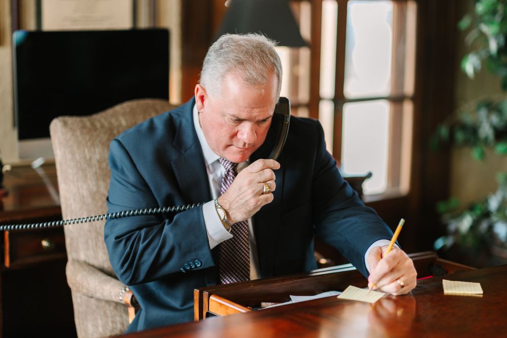 Professional in suit speaking on landline phone while taking notes at desk.