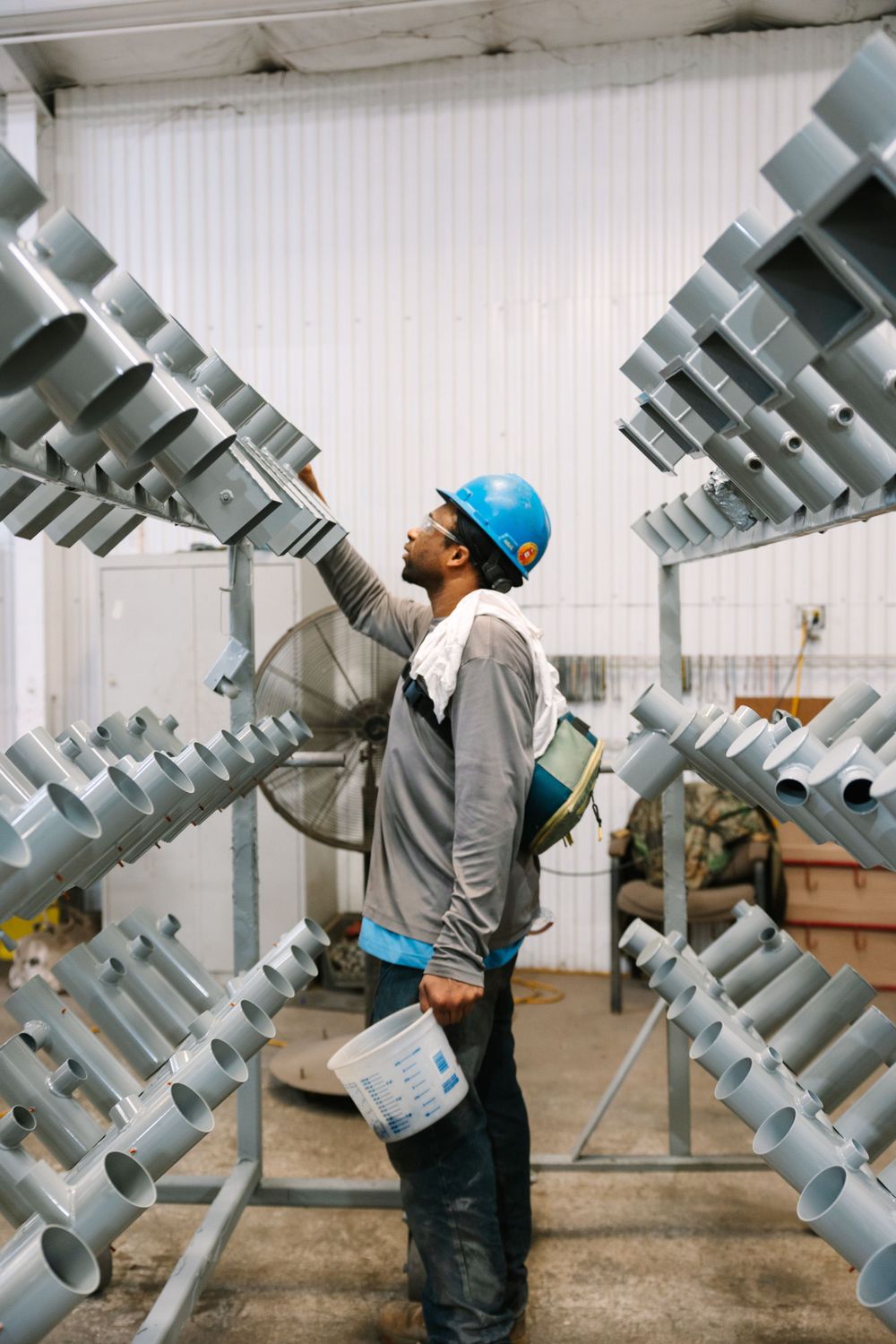 Worker in hard hat inspecting industrial metal structures in warehouse.