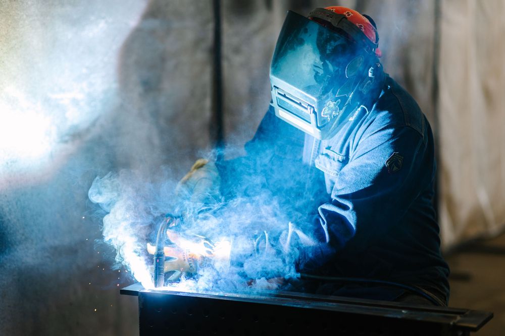 Welder in protective gear creating bright blue sparks while working on metal in a workshop.