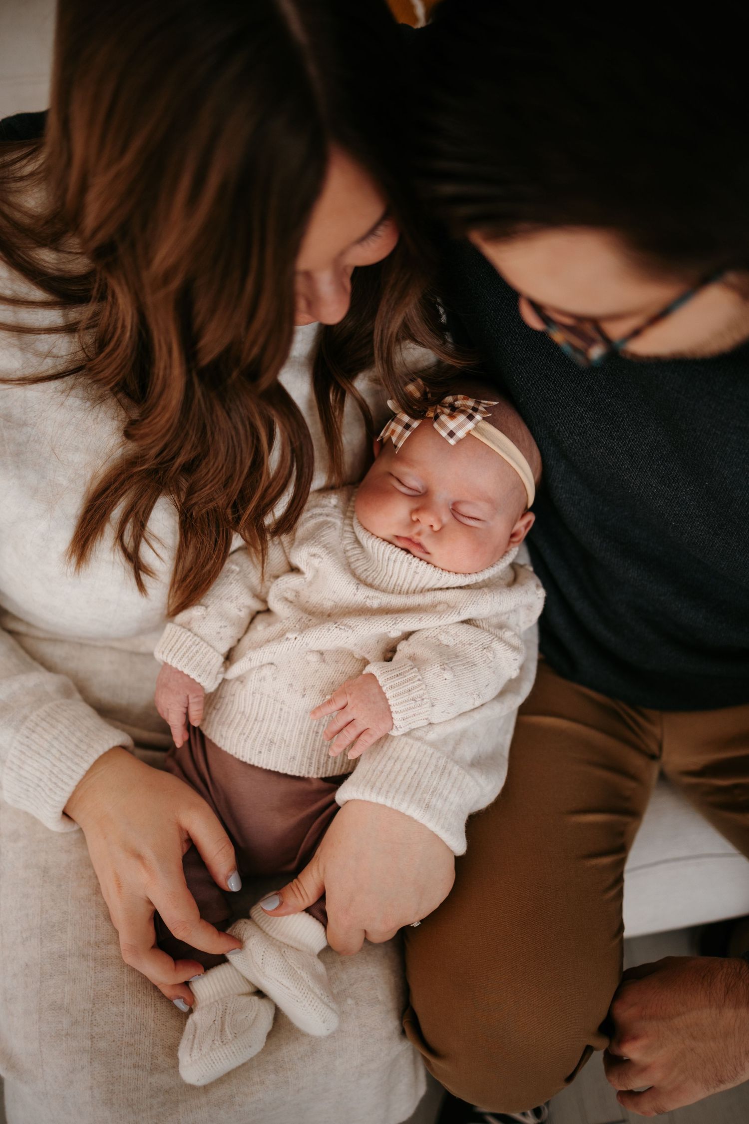 Intimate family moment with newborn baby in cream sweater being held by parents.