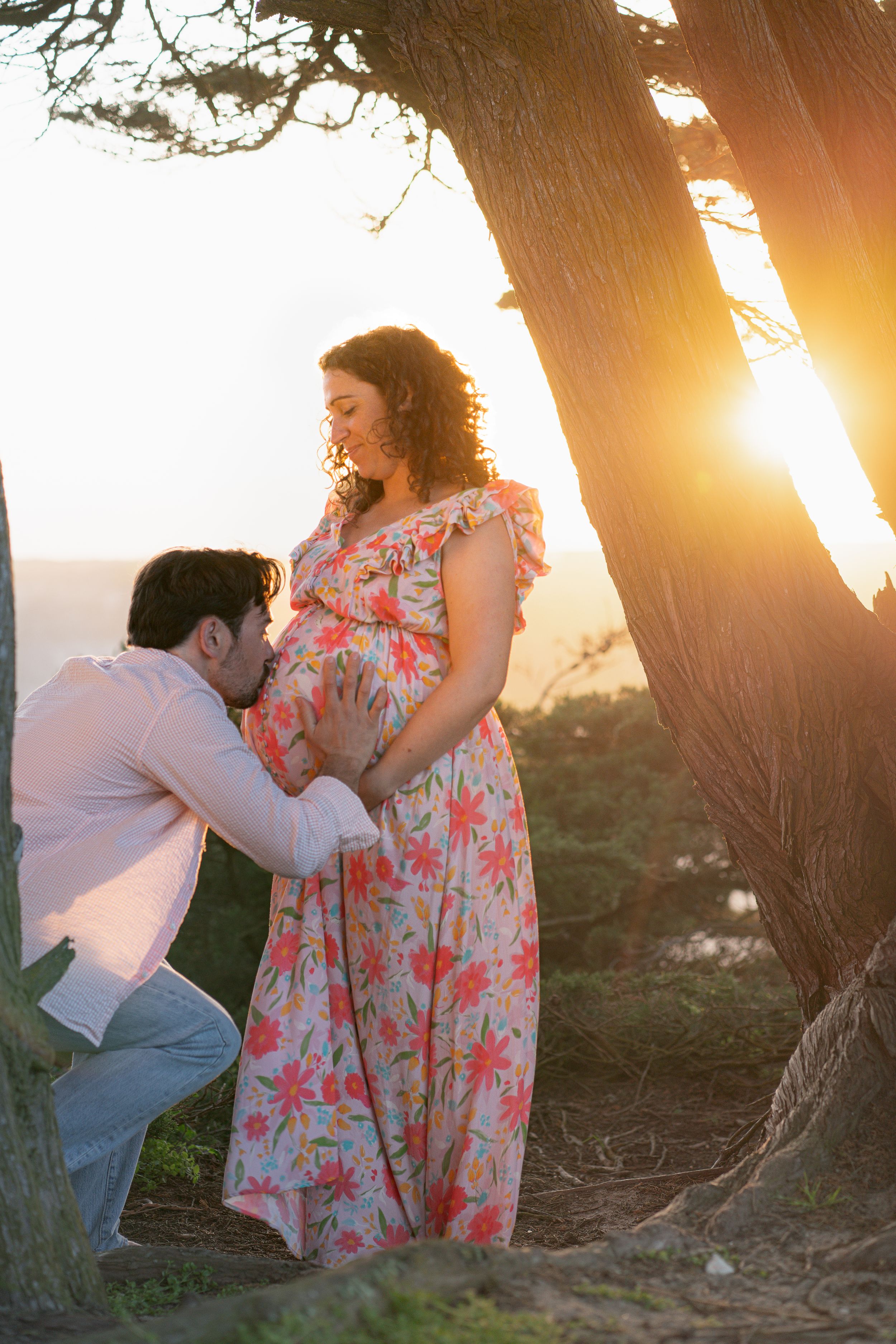 Intimate maternity moment captured at sunset under tree with golden backlight.
