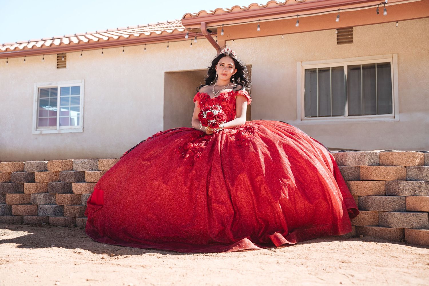 A vibrant red quinceañera ball gown portrait against a rustic stone wall backdrop.