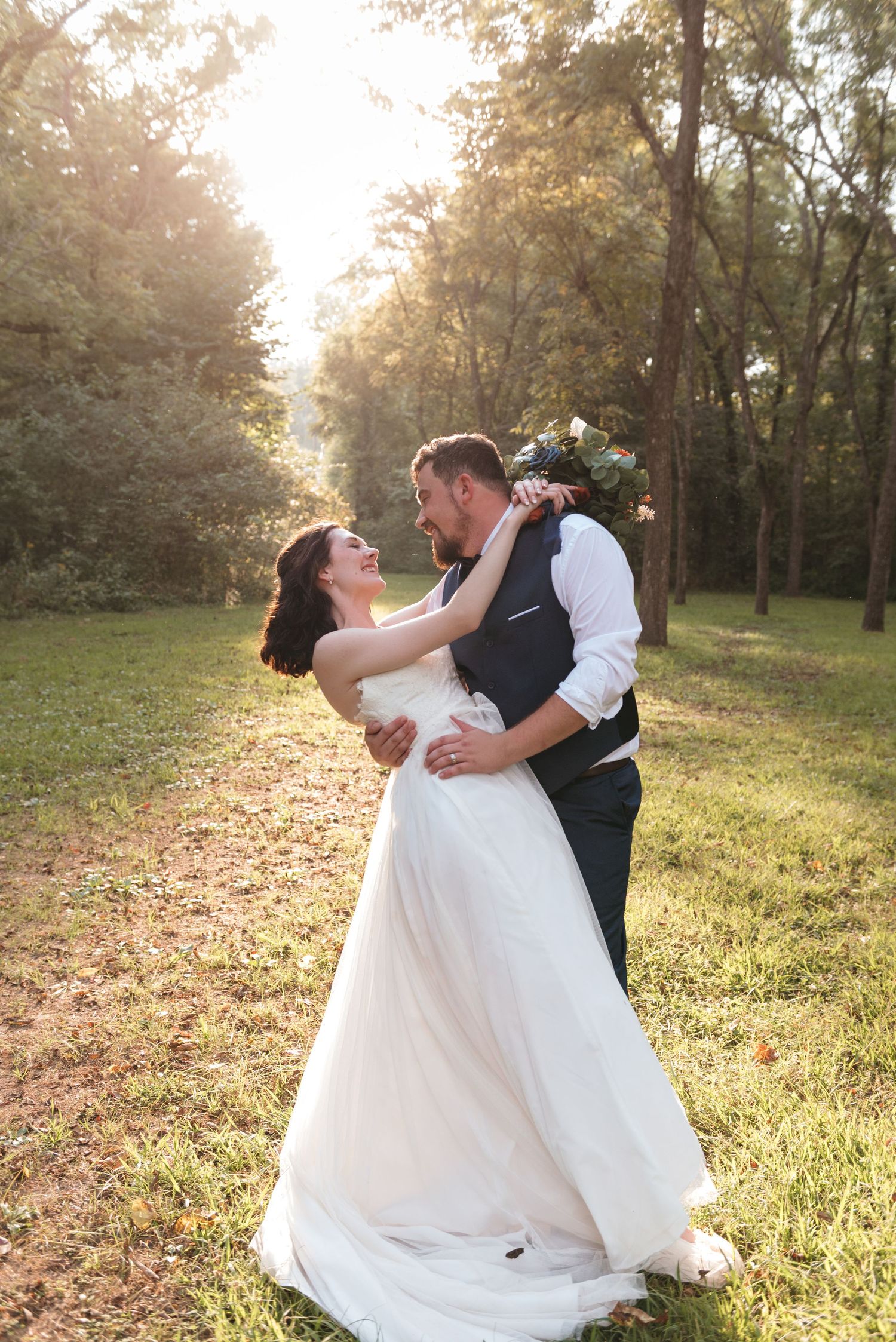 Romantic sunset wedding photo with couple dancing in white dress and vest.