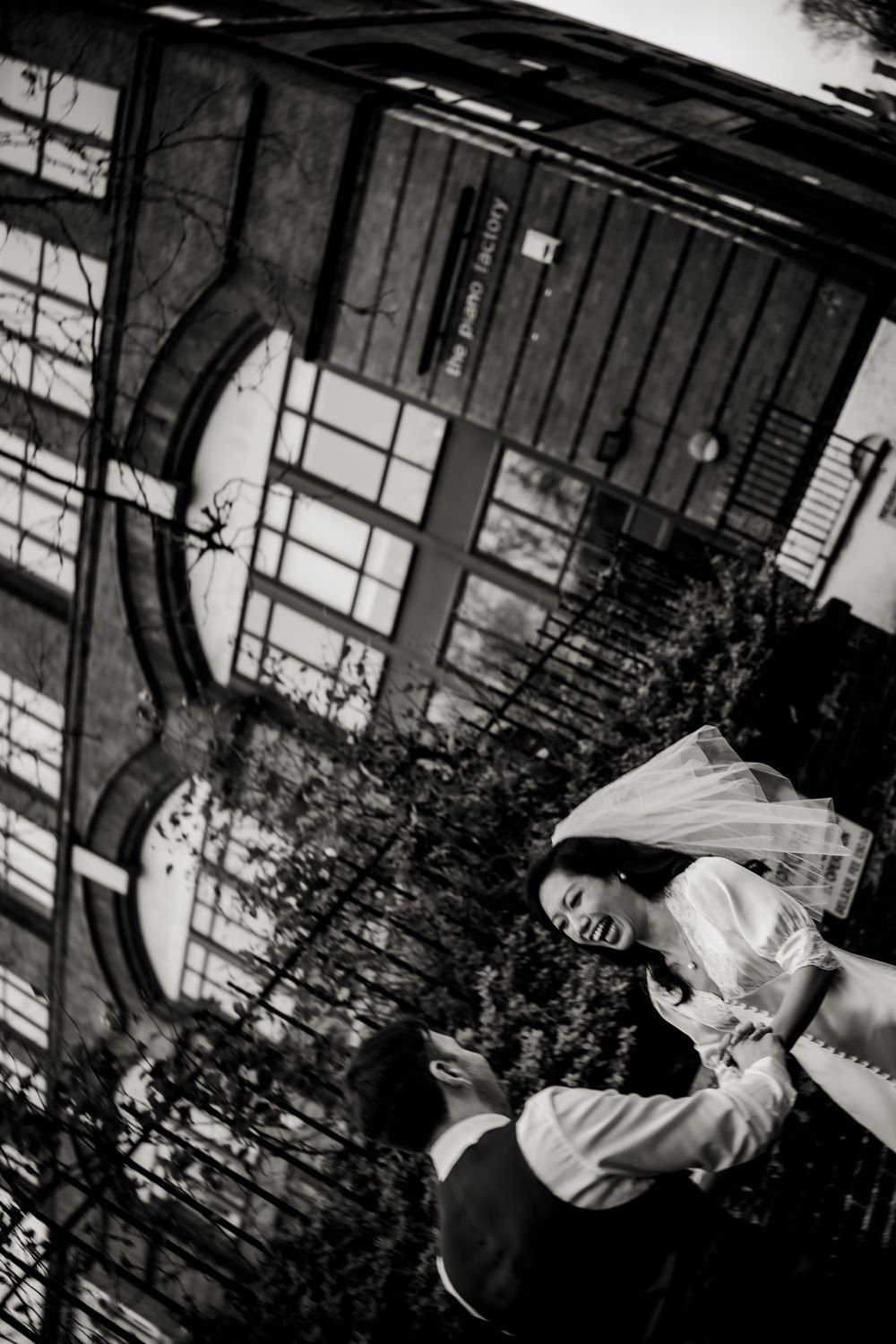 A joyful black and white wedding moment captured under an architectural archway with bushes in the background.
