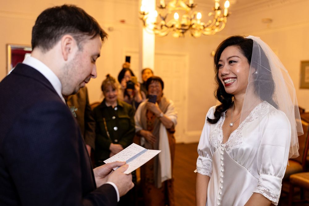 Wedding ceremony in an elegant room with chandelier as couple exchanges vows.