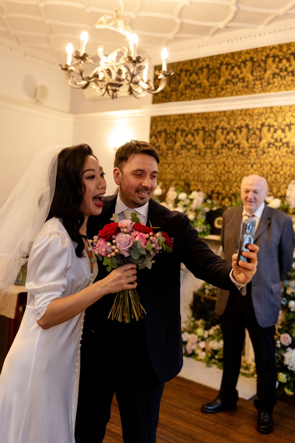 A joyful celebration in an elegant room with a chandelier and ornate wallpaper.