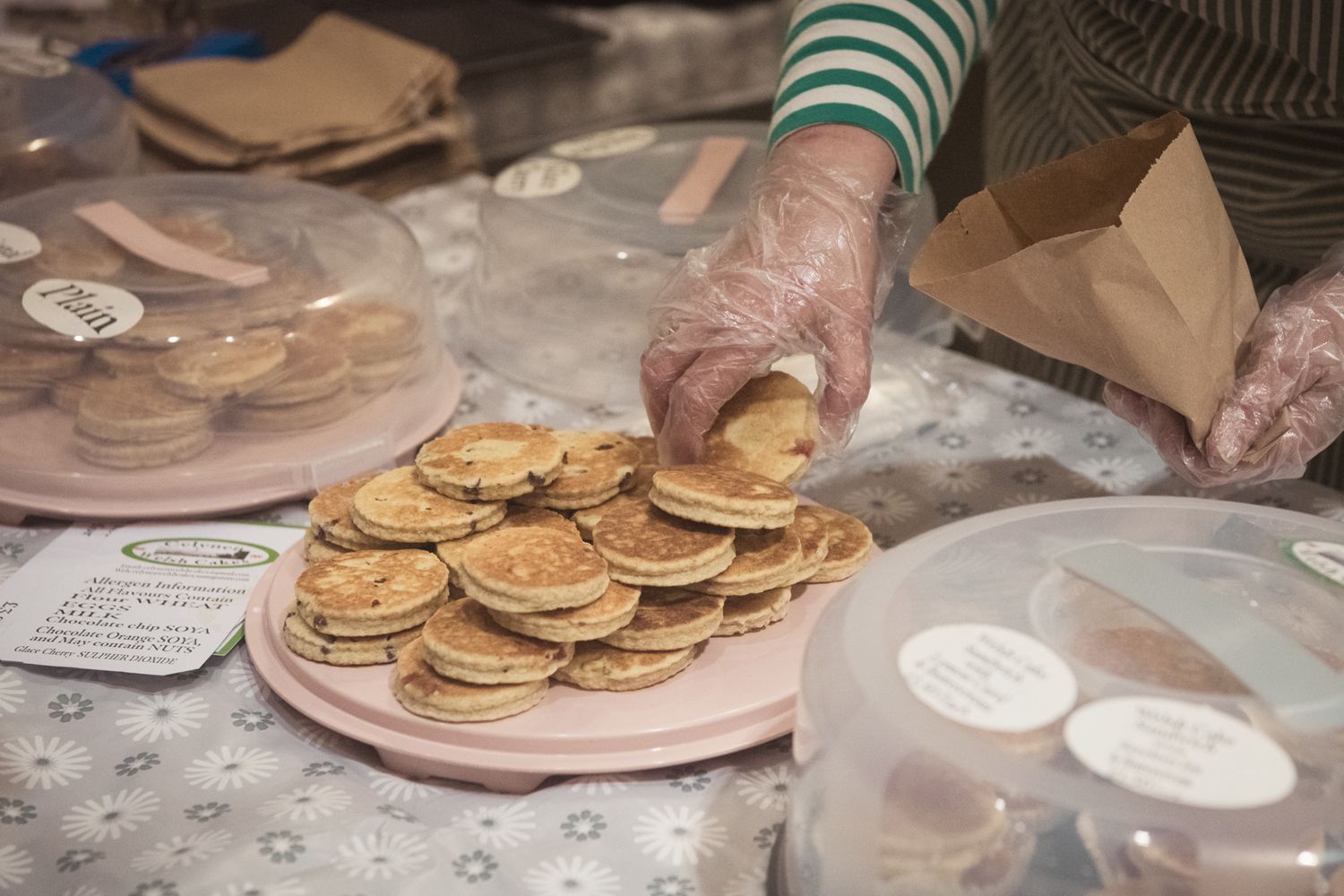 Plate of welshcakes with a hand taking one off the plate and holding a paper bag in other hand. Candid photography by K Lewis photography