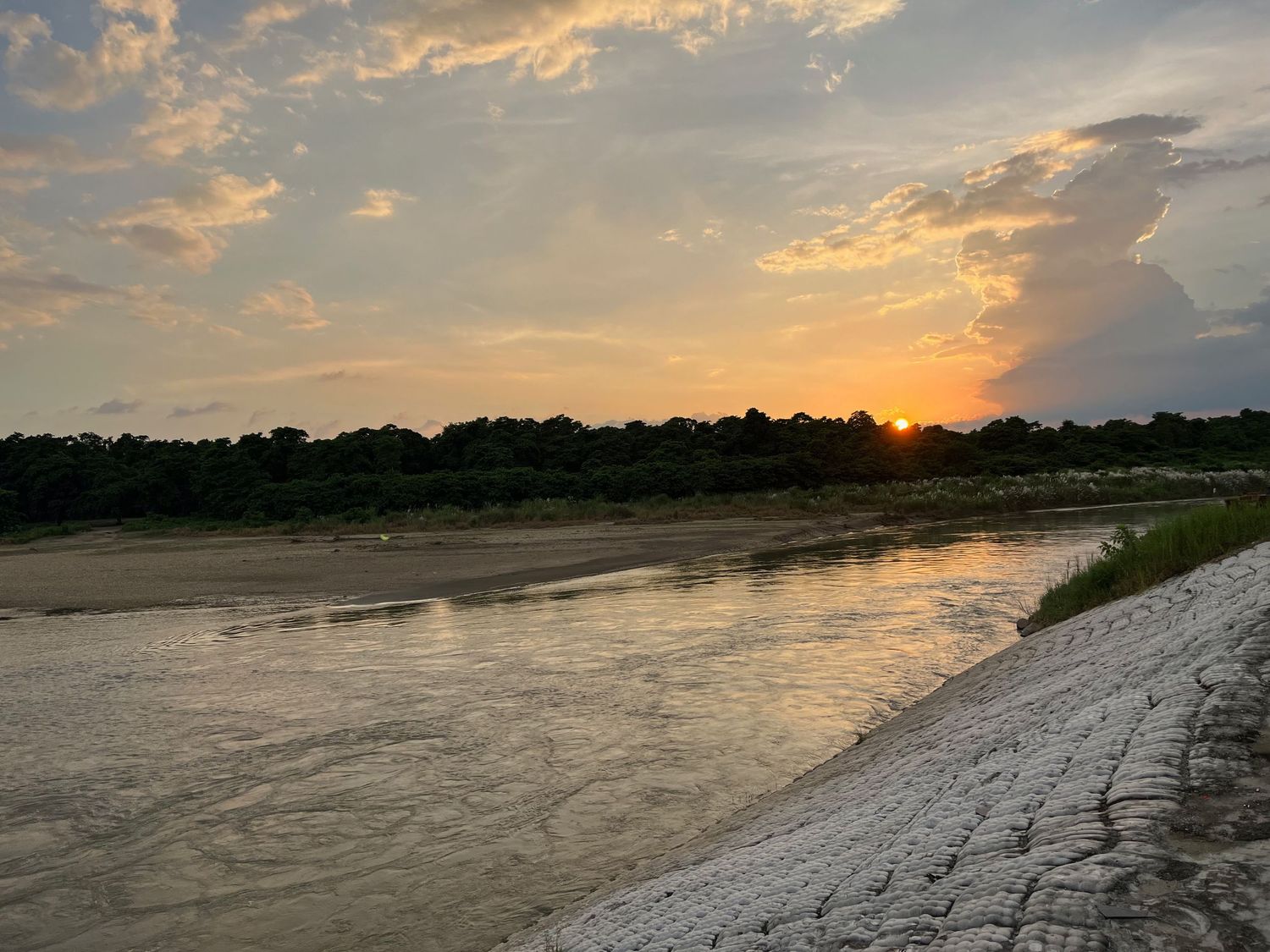 Golden sunset over a river with sandy banks and tree silhouettes on the horizon.