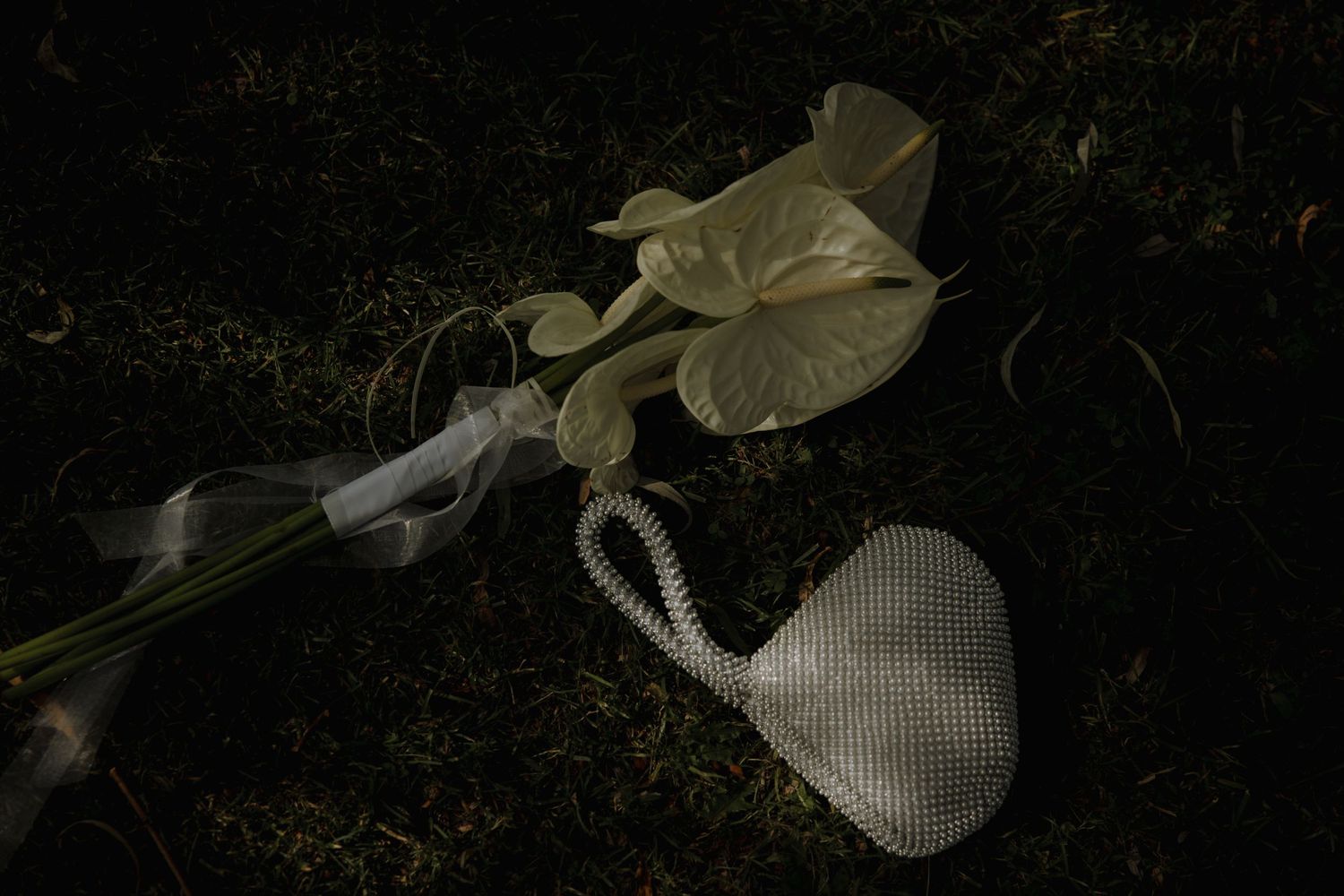 Artistic still life of a white flower and beaded purse in dark lighting.