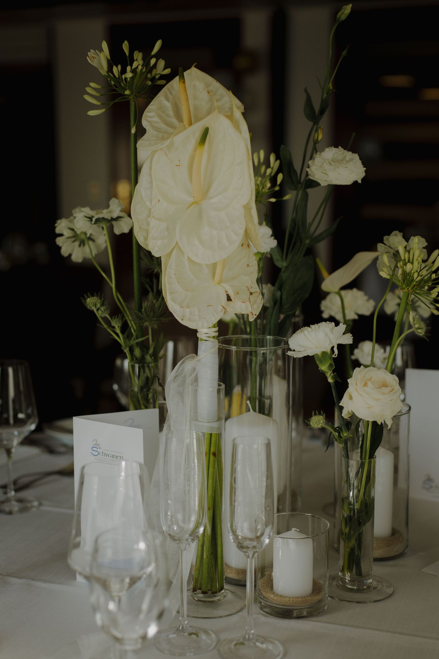 Elegant white floral centerpiece with anthurium flowers and glass candleholders on a table.