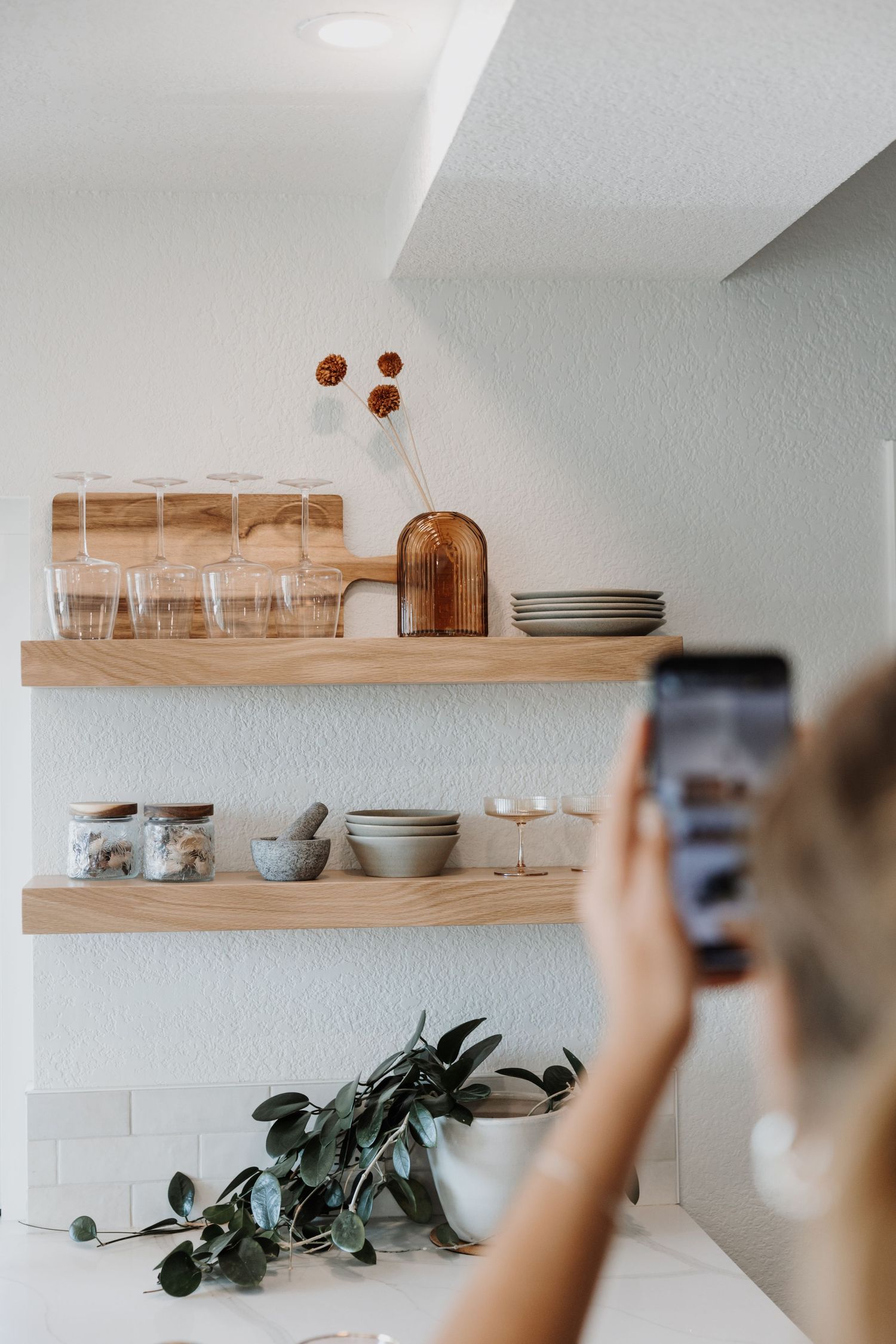 Minimalist kitchen interior with wooden floating shelves displaying dishes and glassware.