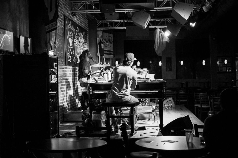 Black and white image of a dimly lit bar or restaurant interior with industrial lighting fixtures.