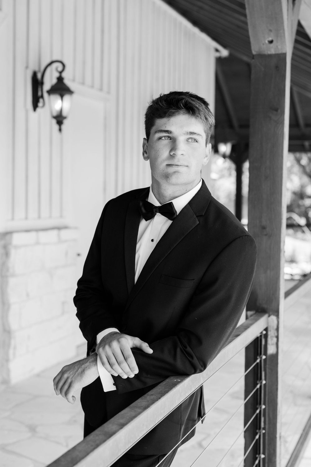 A formal portrait of the groom in a black tuxedo standing on a porch with white columns.