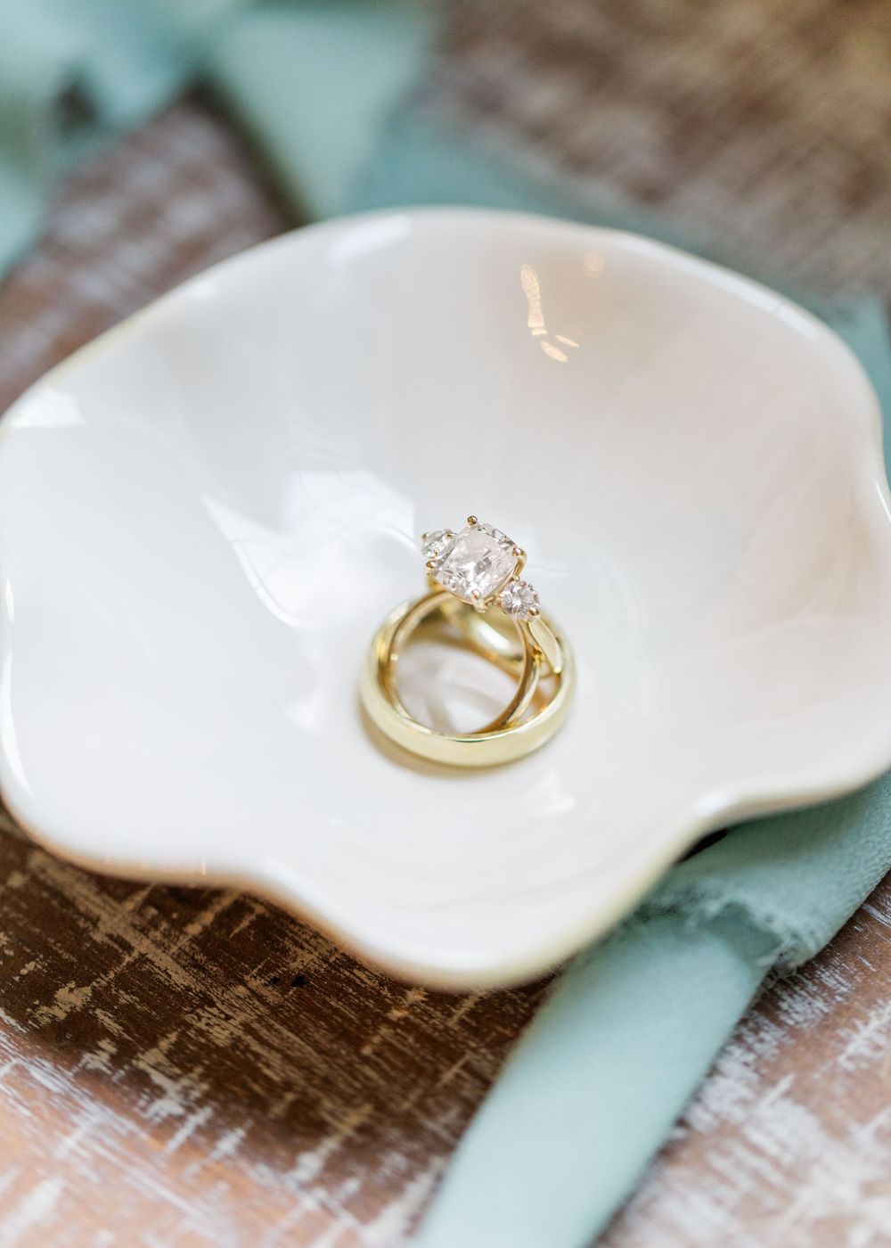 Gold wedding rings nestled in a white ceramic dish with textured background.