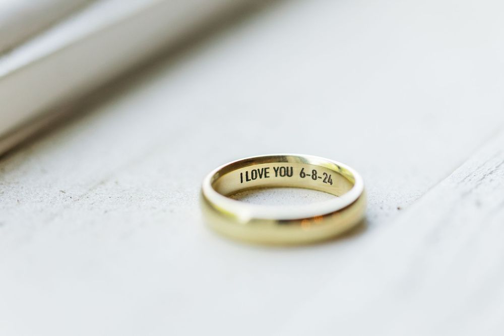 Gold wedding band with engraved message photographed on white surface.