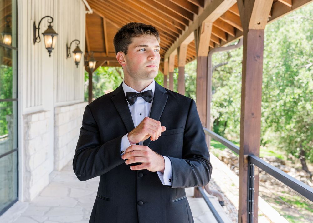 Groom adjusting cufflinks on covered porch during wedding preparations.