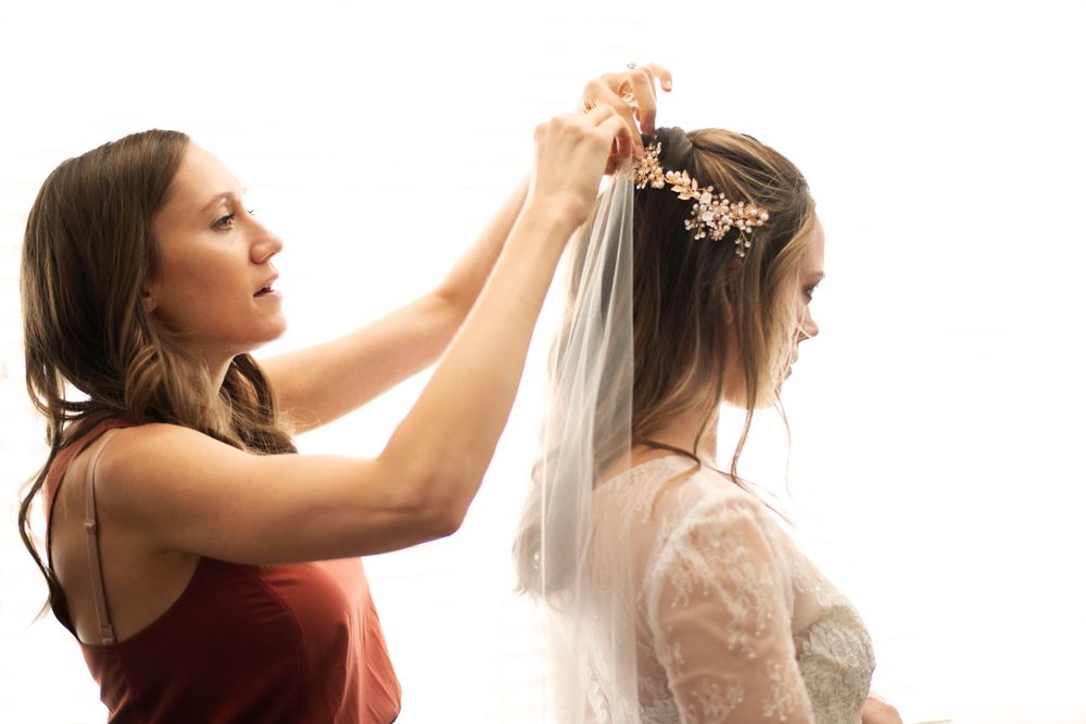 Bride getting ready wedding photo. Maid of honor helps bride with veil. Classic timeless bright romantic beautiful lighting. Wedding dress