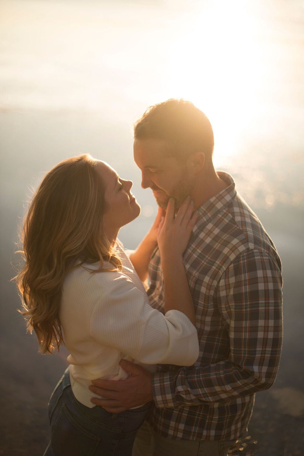 Golden hour sunset engagement photos by lake. water sparkling sunset reflecting off water. hands on fiance's neck. Sweet intimate romantic