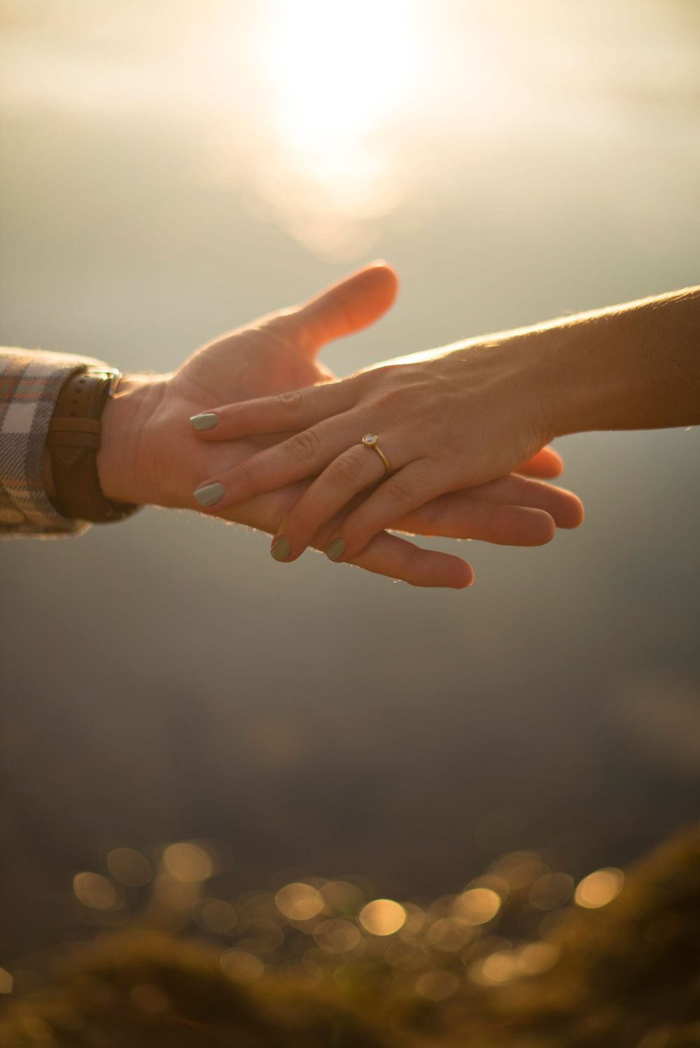 Golden hour sunset engagement photos. Holding hands by lake showing engagement ring, the water sparkling and sunset reflecting off water.
