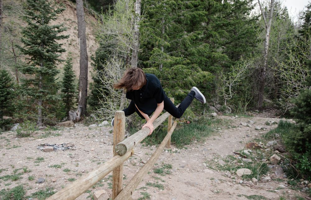 Person performing acrobatic jump over wooden fence on mountain trail.