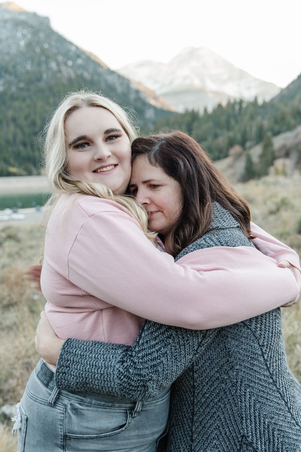 Two people sharing warm embrace outdoors with mountain landscape behind them.