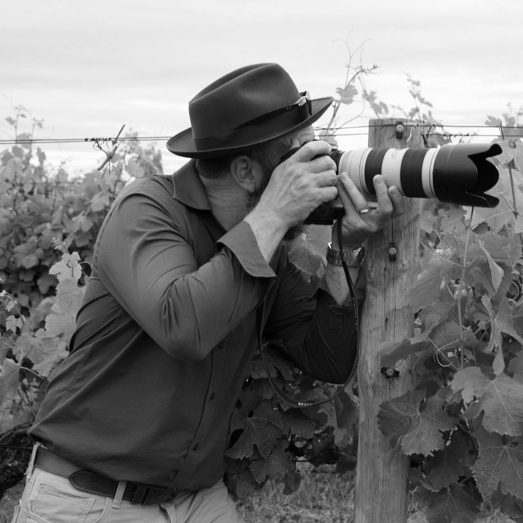Jason Robins taking photos in the vines at S.Leonards Vineyard with a Canon Camera, wearing a Akubra hat.