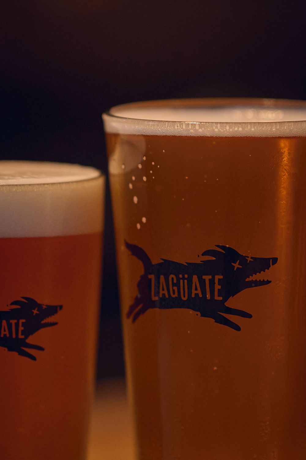 Two beer glasses with Lagunate logo showing amber and light colored craft beers with foamy heads.