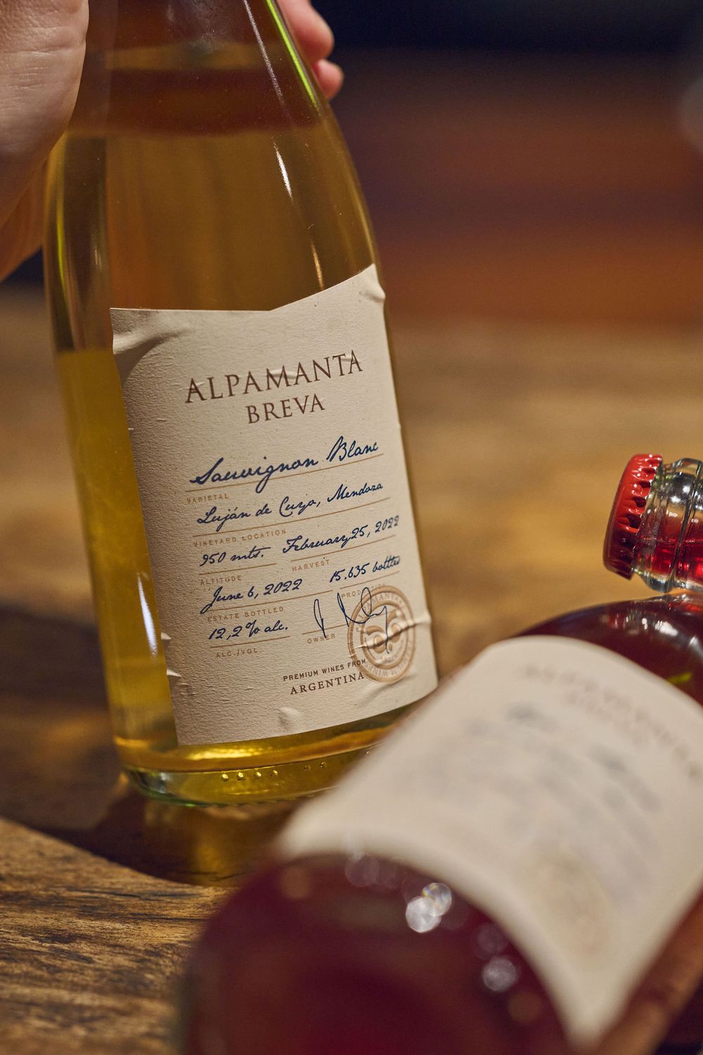 Close-up details of wine bottle labels showing Alpamanta and Breva varieties on rustic wooden surface.
