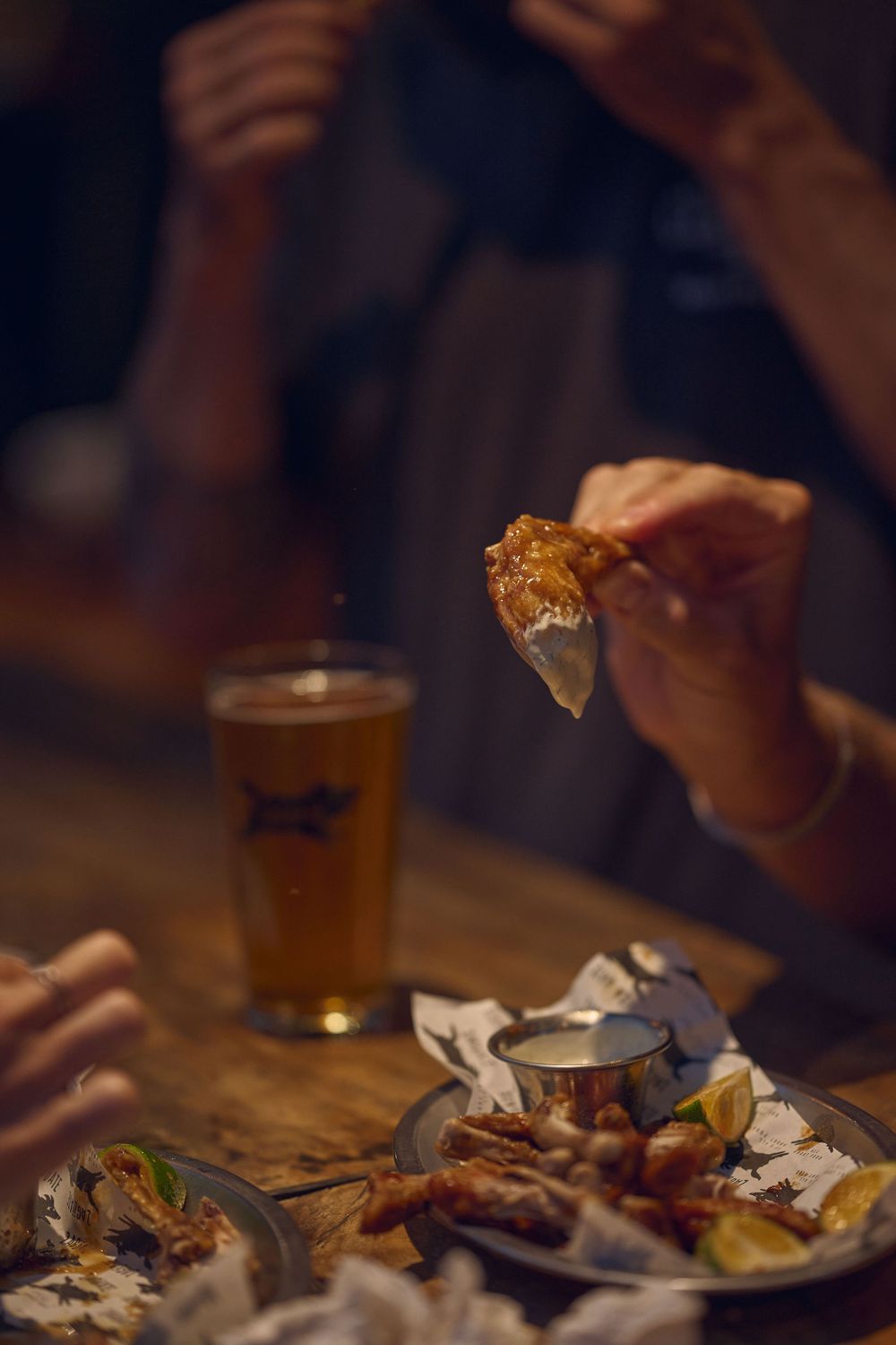 Friends enjoying craft beer and appetizers at a dimly lit bar table with shared plates and glassware.
