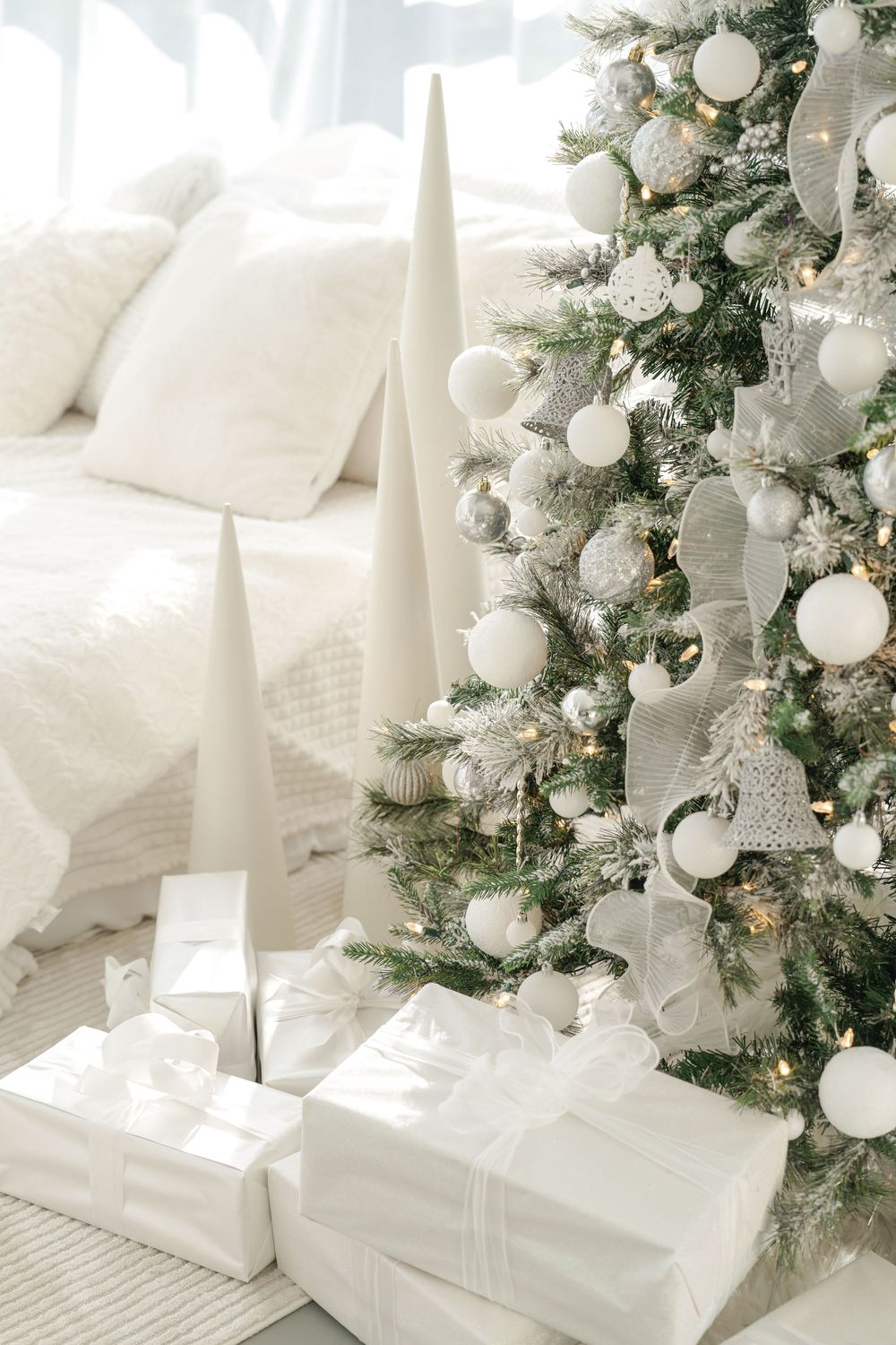 Elegant Christmas tree with white and silver decorations creates a serene winter display next to wrapped gifts.