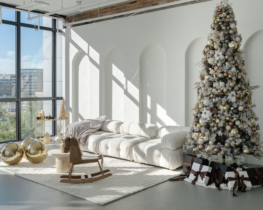 A modern white living room with floor-to-ceiling windows, decorated with an elegant flocked Christmas tree and rocking horse.