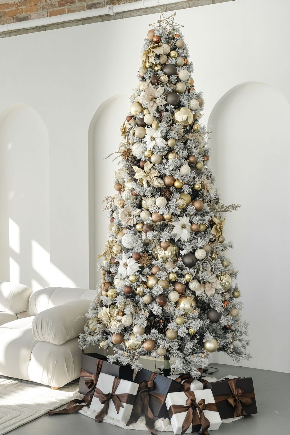 Flocked white Christmas tree decorated with silver and gold ornaments and wrapped presents underneath.