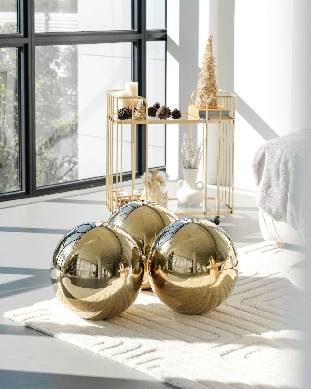 Large metallic gold Christmas ornaments and golden candle holders arranged on a white surface in natural lighting.