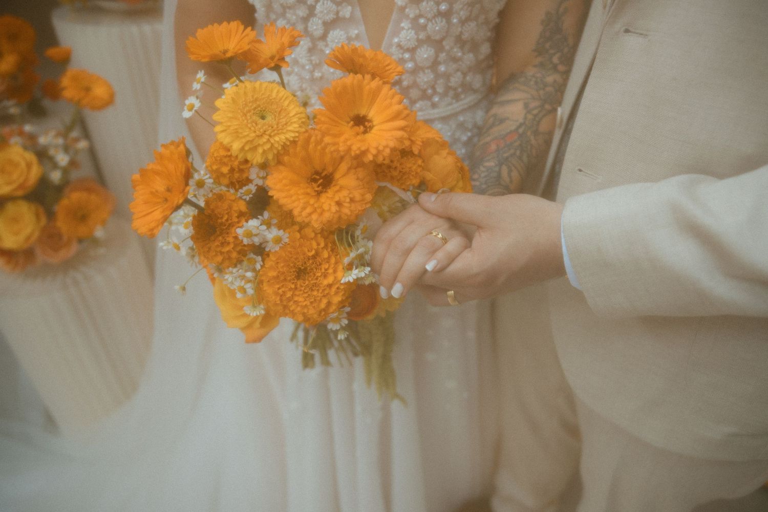 Couple shares romantic moment on modern patio couch with orange pillows against abstract wall mural at wedding venue.