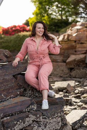 Woman business owner Talks Over Tea Mental Health Therapist in Tacoma, WA personal branding  sitting on beach rocks in pink jumpsuit