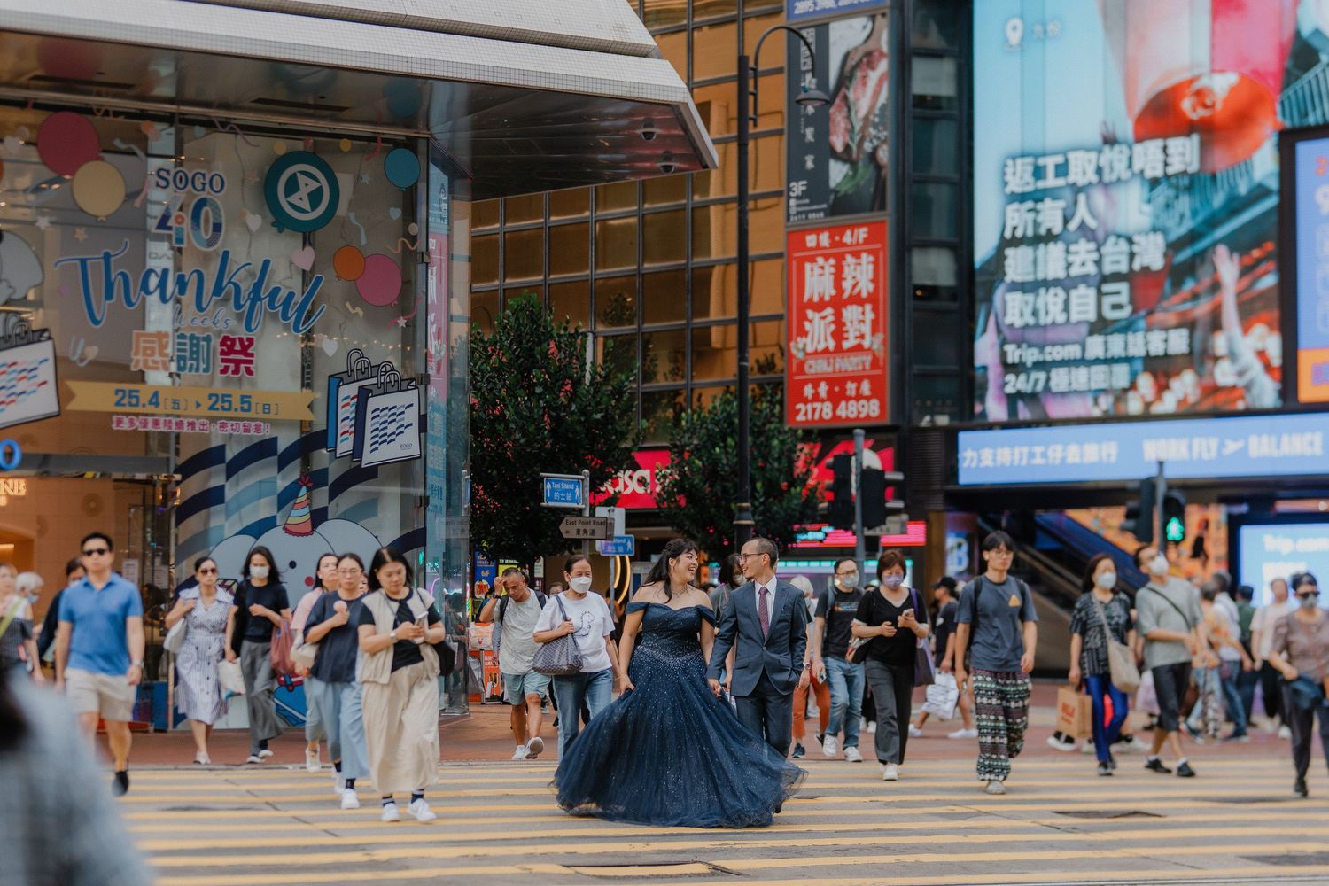 Busy urban scene with pedestrians walking on streets in Hong Kong, surrounded by storefronts with Chinese signage.