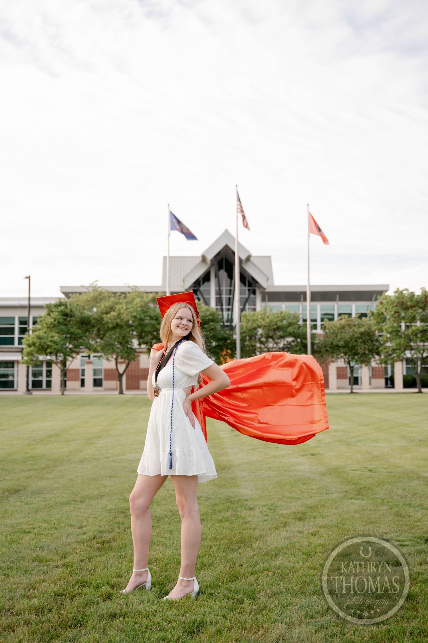 A graduation photoshoot series on a grassy lawn with modern campus buildings in the background on a cloudy day.