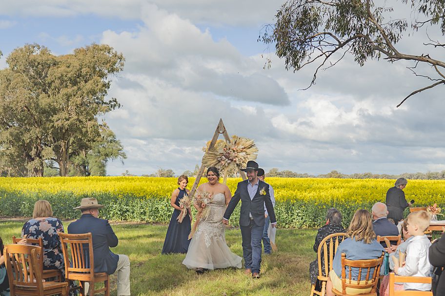 Wedding party poses for photos in vibrant yellow canola field with gum trees and cloudy sky in the background.