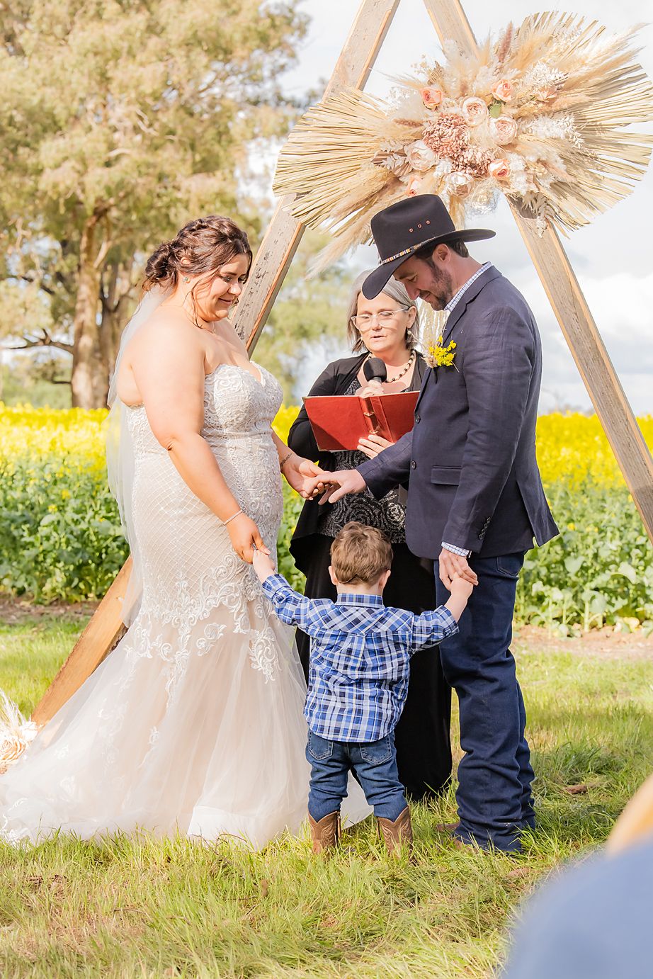 Couple shares an intimate moment during their outdoor wedding ceremony surrounded by wooden decor and yellow wildflowers.