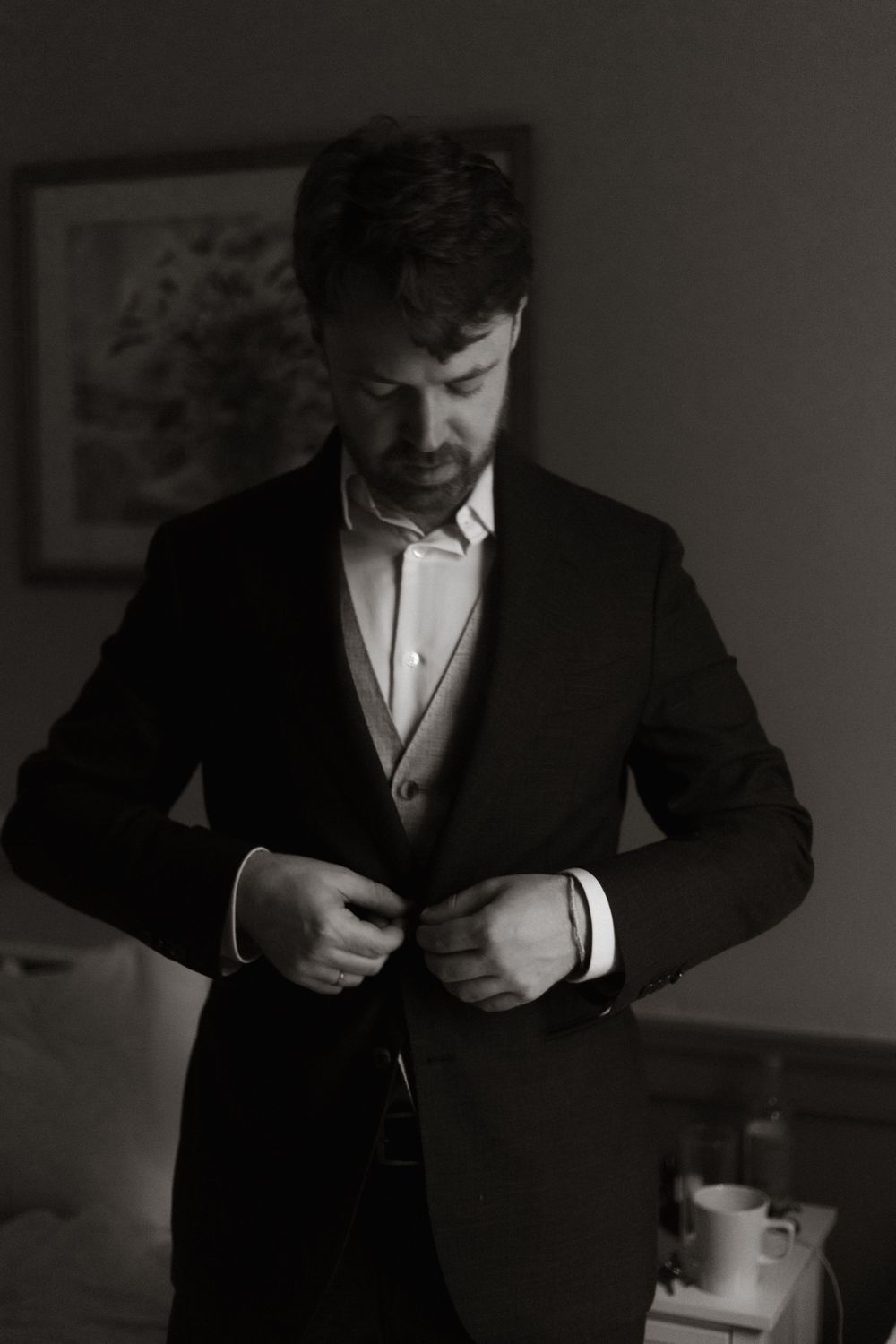 A person in a dark suit buttoning up their jacket in a black and white photograph.