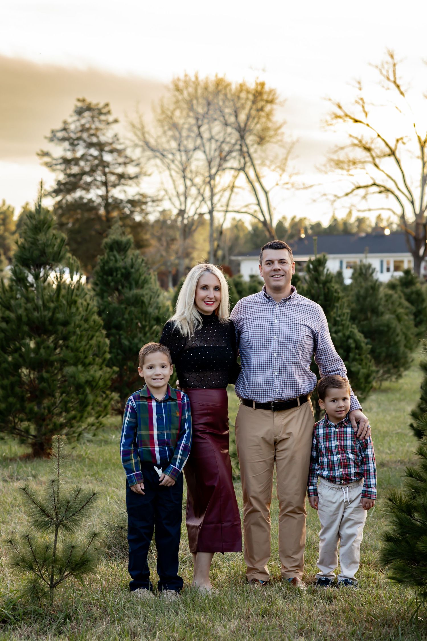 A family stands together at a Christmas tree farm during golden hour among evergreen saplings. Fall family photographer in Richmond, VA