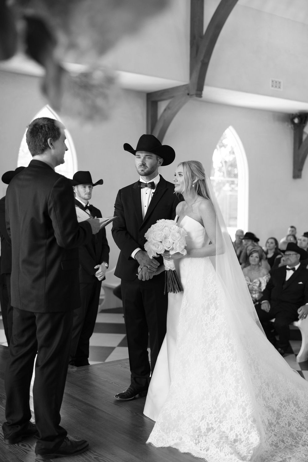 A black and white wedding ceremony takes place inside a church with arched windows and wooden beams.