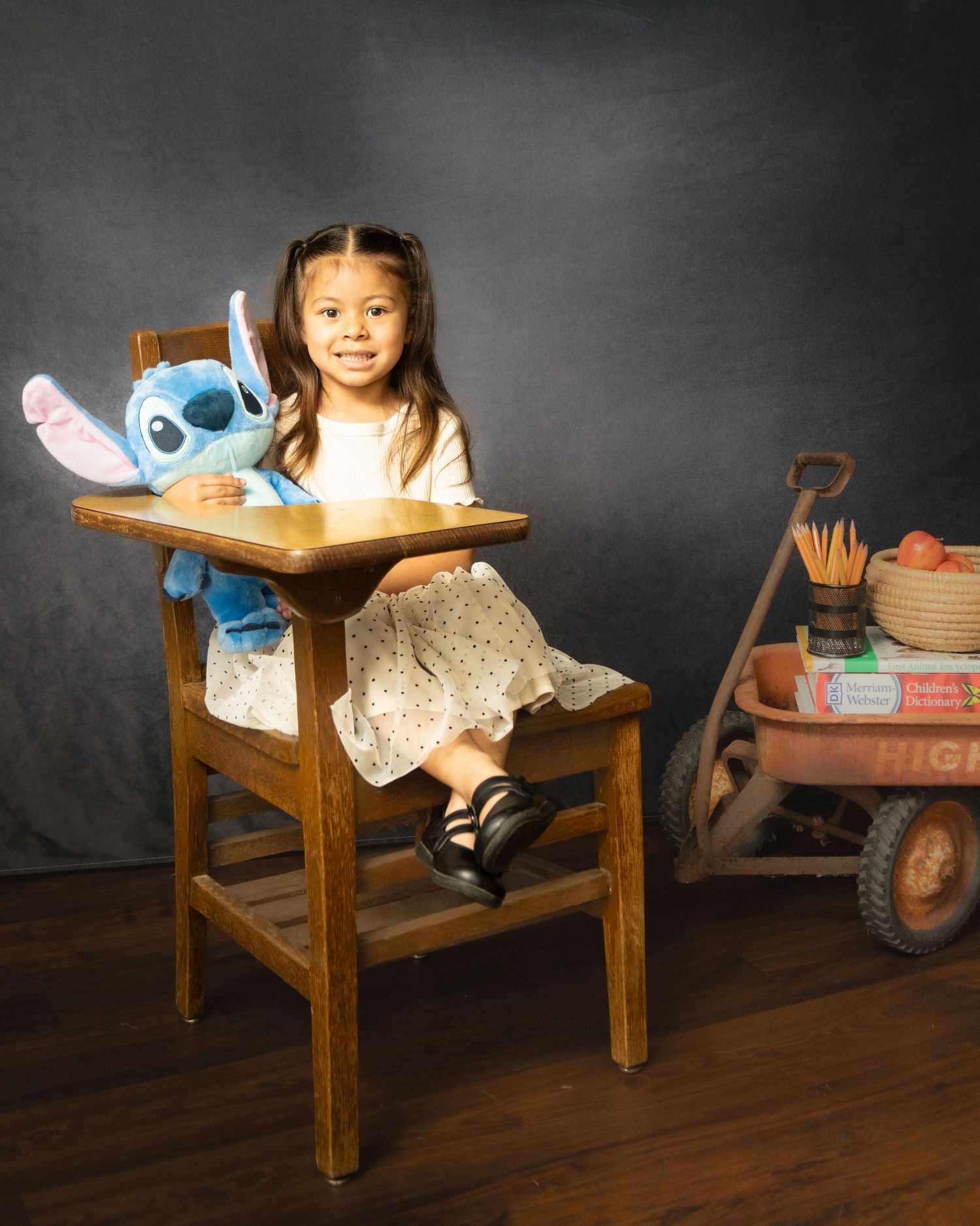 A wood desk chair in a dark room holds a blue Stitch plush toy and shows a child at study time.