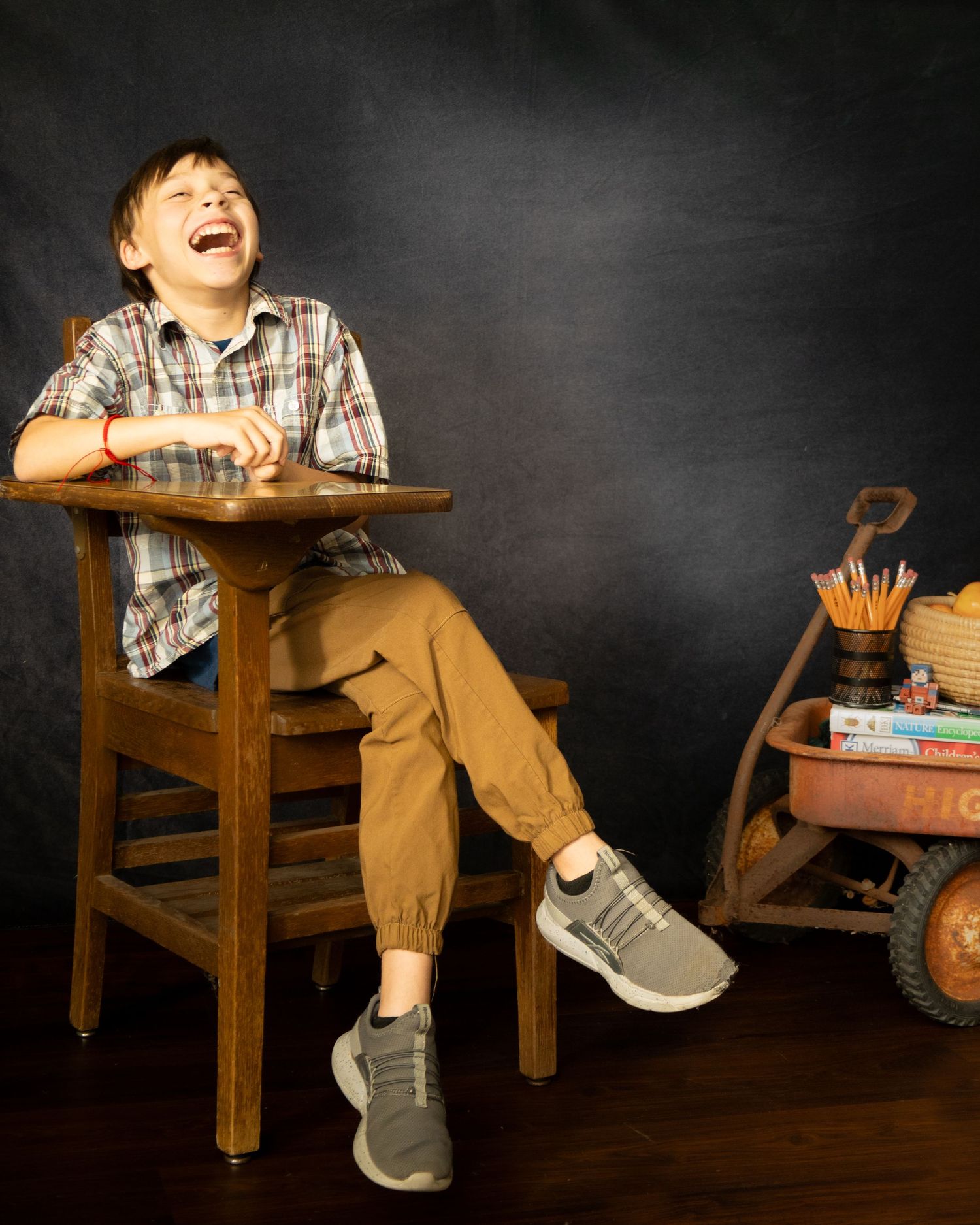A child sits at a wooden school desk against a dark chalkboard background, showing various expressions of laughter and joy.