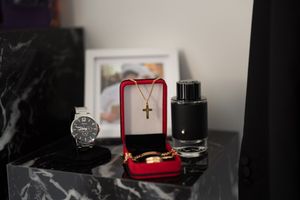 Wedding accessories including a watch, cross necklace, and rings displayed on dark marble.