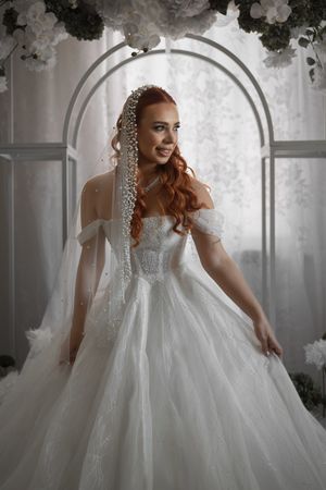 A bride in a princess ball gown poses under a floral arch with delicate veil details.