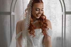 A bride in an embellished ball gown smiles while wearing an ornate crystal-trimmed veil.